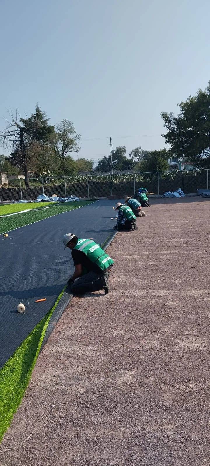 Instalador pegando las uniones del pasto sintético con cinta y adhesivo en una cancha
