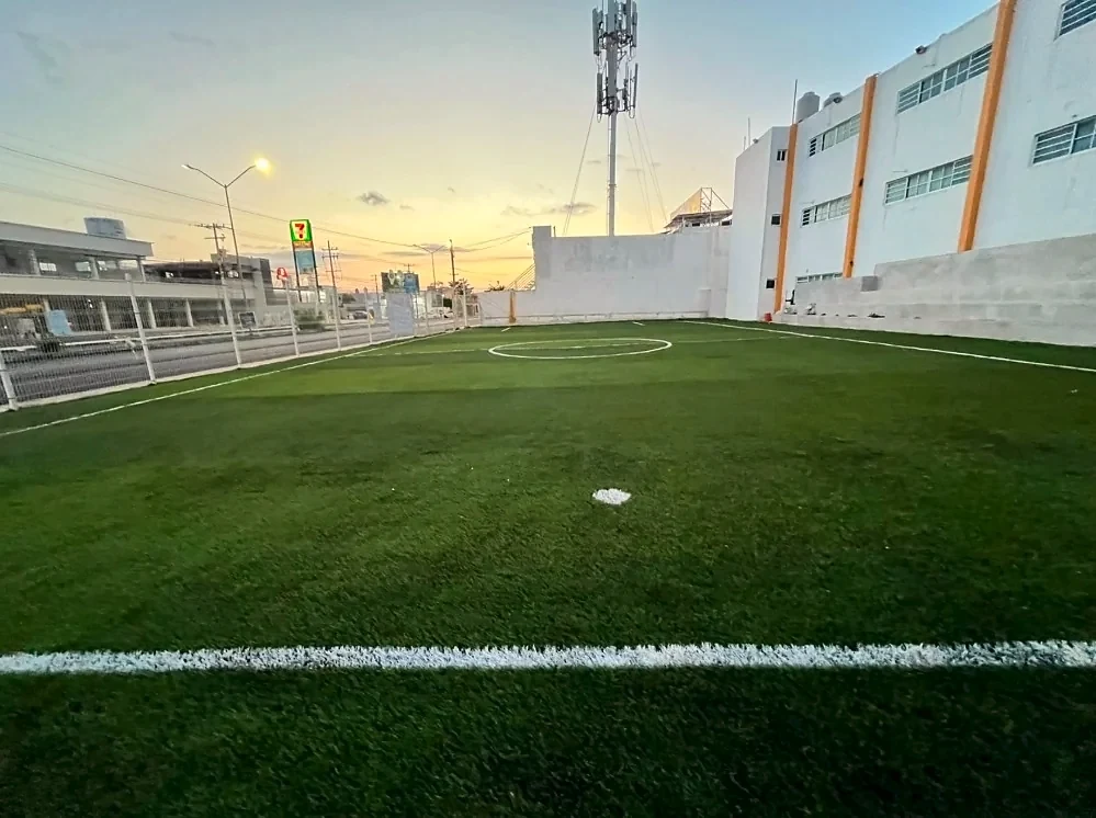 Círculo central y línea media de una cancha de pasto sintético entre los edificios de un colegio en Mérida, Yucatán