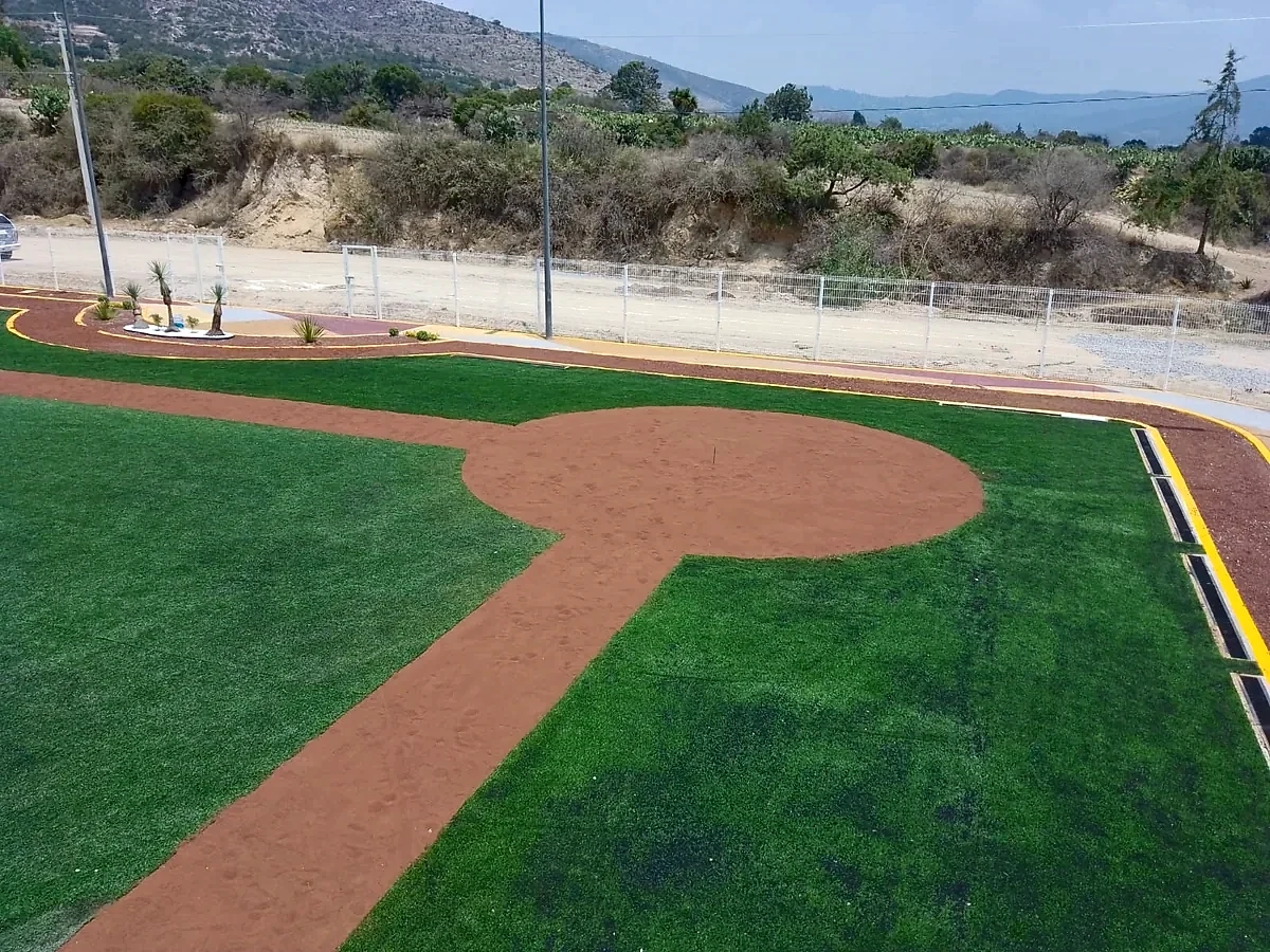 Círculo de home y camino al montículo en arcilla sobre pasto sintético en el campo de béisbol de Santiago Tenango, Puebla