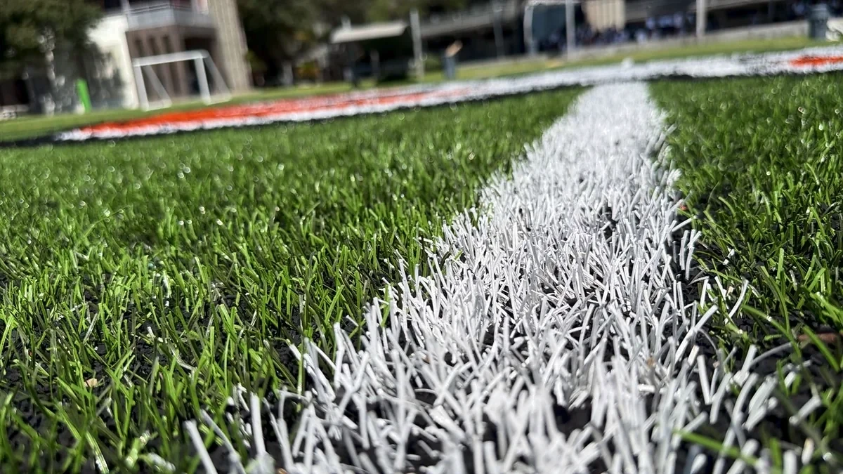 Detalle de la fibra del pasto sintético y de una línea blanca insertada en la cancha de un colegio en Reynosa