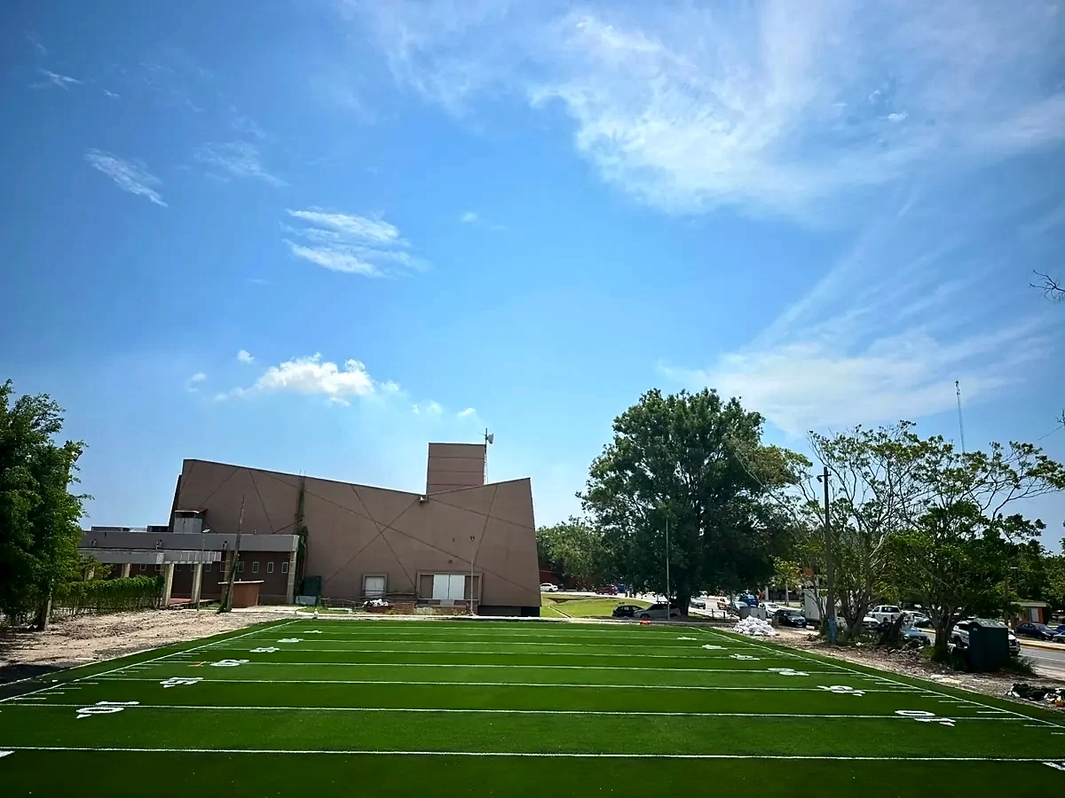 Campo de pasto sintético con líneas de yardas y el edificio de la facultad al fondo en la UAT Facultad de Derecho, Tampico